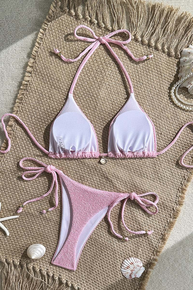 Pink and white thong bikini set on a textured surface with seashells.