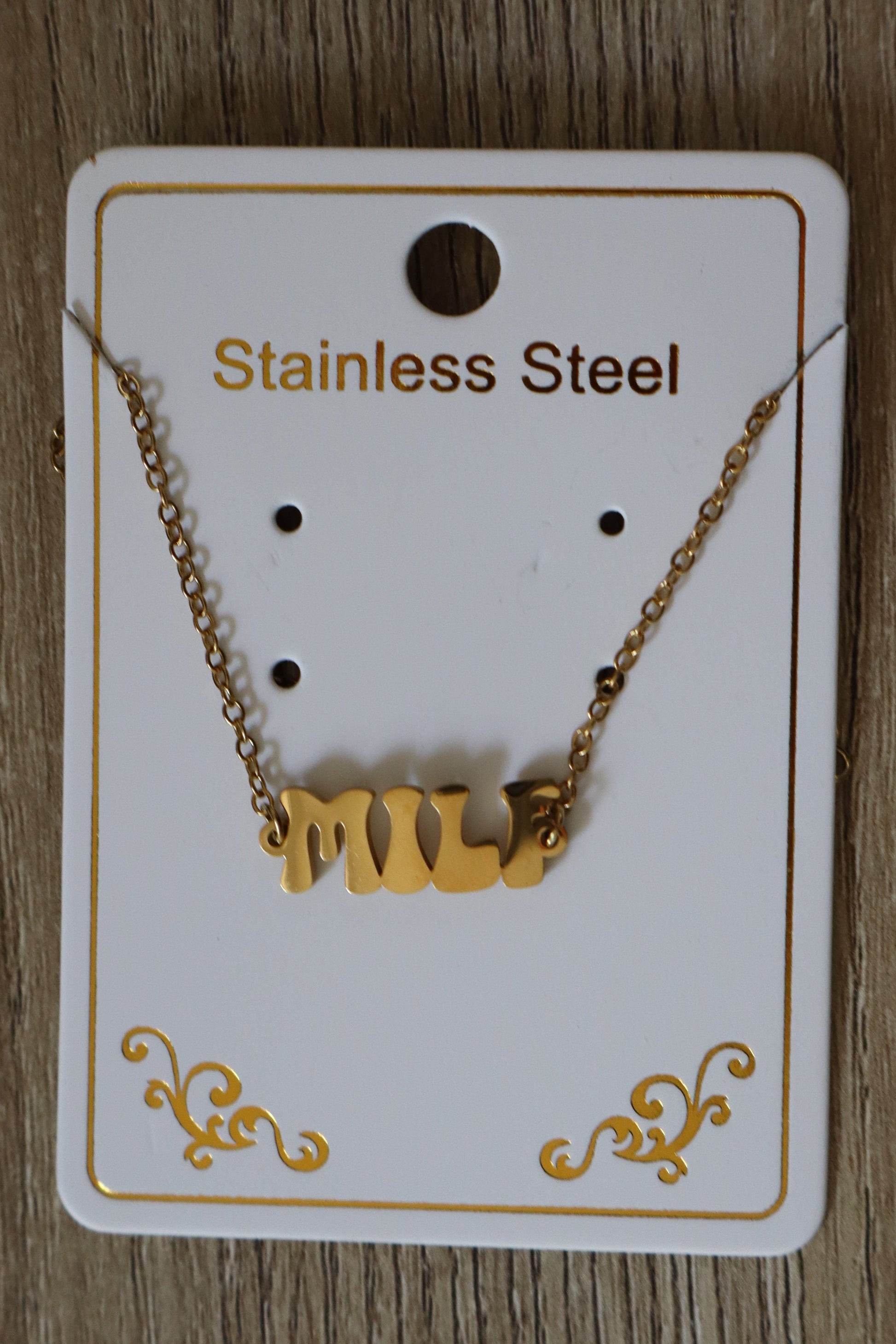 Gold anklet / bracelet on a white card with 'MILF' Logo charm, on a wooden surface